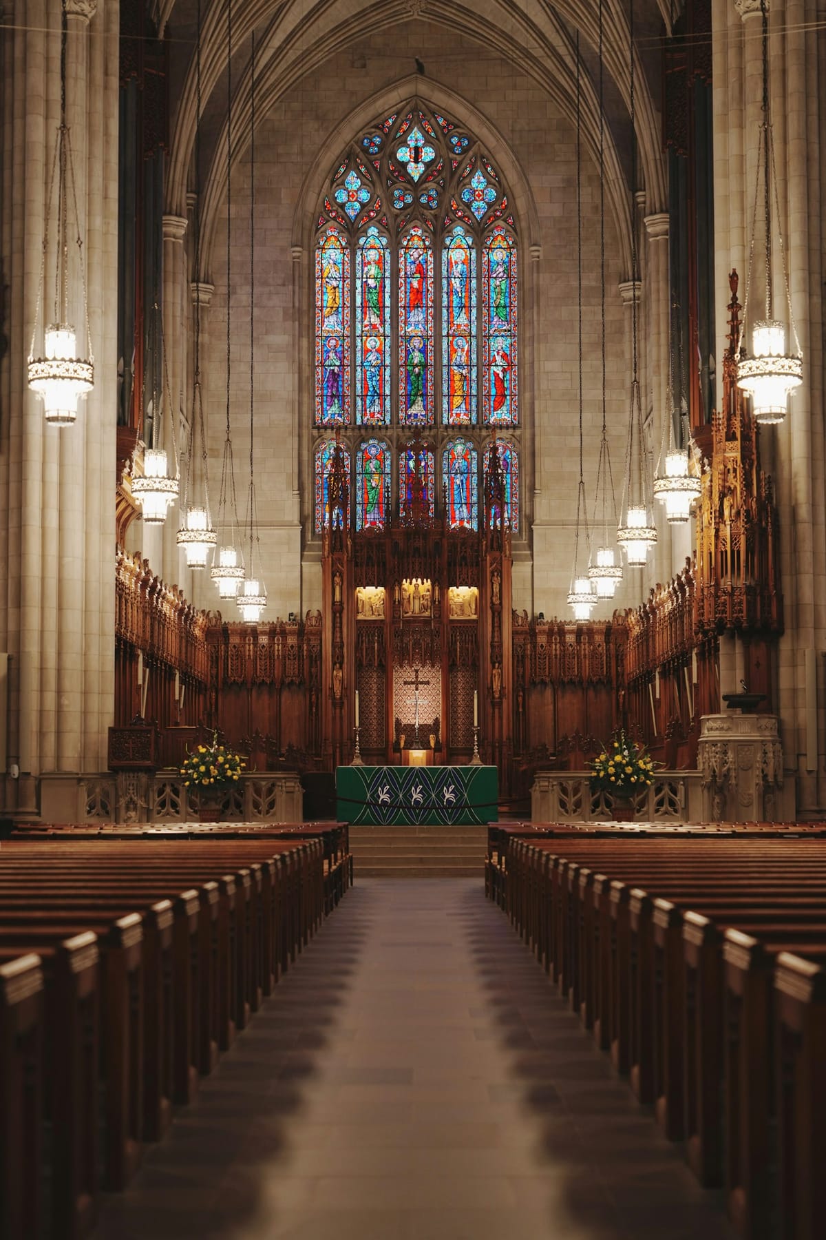 Rows of wooden pews leading to a stained glass window and altar