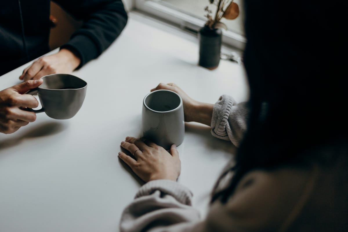 Two people talking over mugs at a table, a mentoring conversation